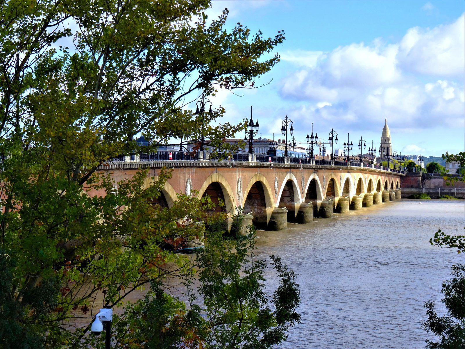 Panoramic view of the Pont de Pierre, a historic bridge spanning the Garonne River in Bordeaux, France, under a clear sky.