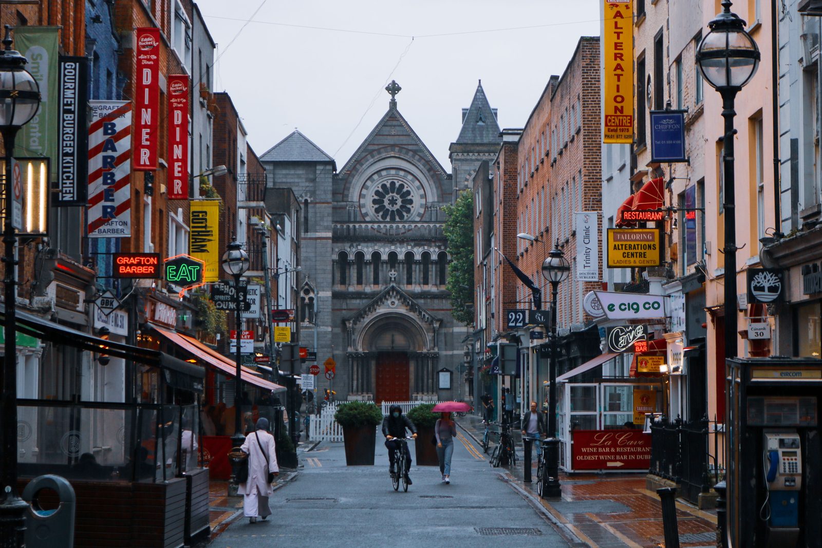 Vue d'une rue animée à Dublin avec l'église de Saint Anne et des magasins. Des gens marchent sous la pluie.