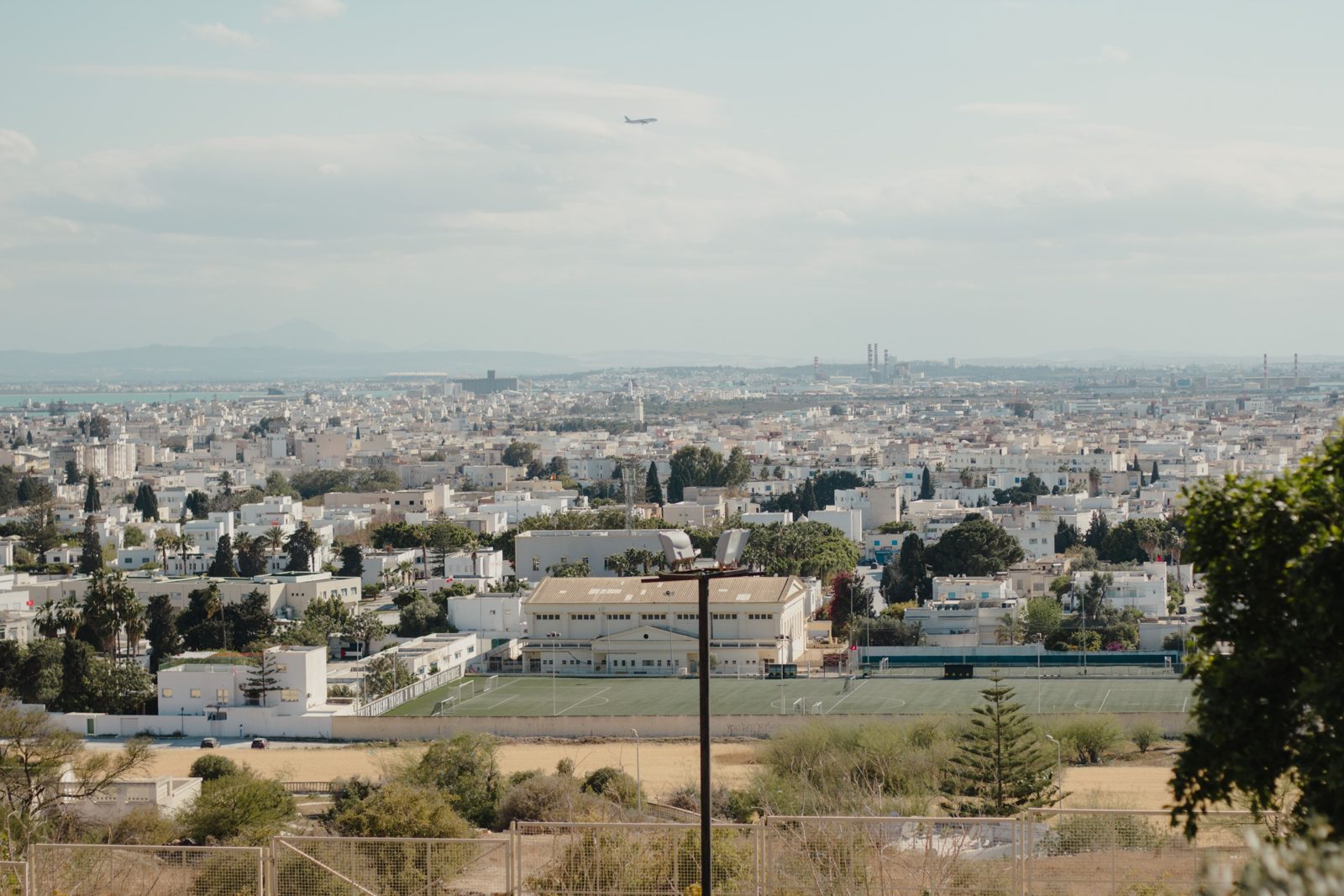 Aerial view of Tunis with a plane in the sky, revealing urban buildings and greenery.